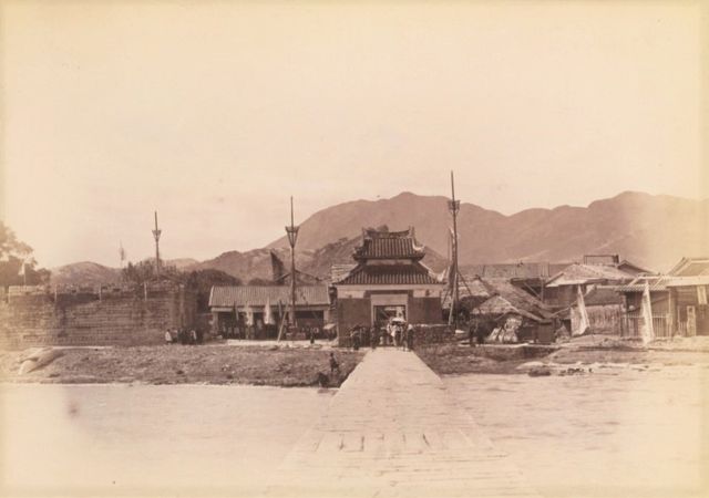 Old sepia photograph of a stone causeway leading to a Chinese pavilion with low hills behind, 1898.