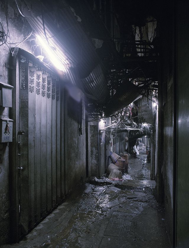 A narrow, wet alley under pipes and cables, lit by fluorescent light, 1993.