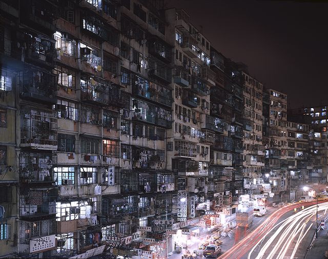 Night photo of a towering wall of lit windows above a street with light trails, 1993.